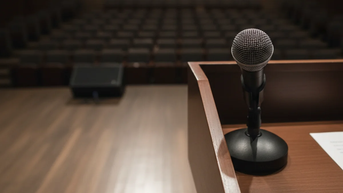 Una silueta d'una persona parlant davant d'un faristol en un auditori buit, simbolitzant una conferència.