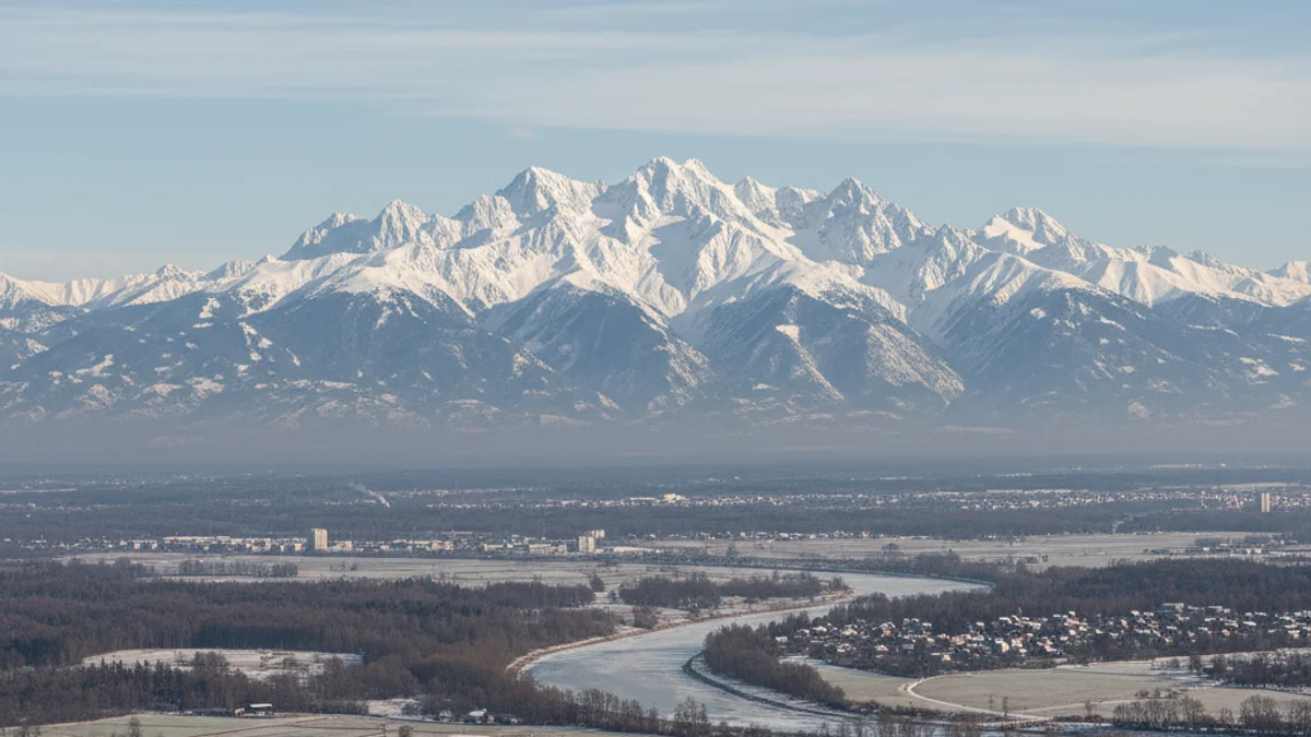 Vista panoràmica d'una muntanya nevada imponent, amb un cel clar i aire net, visible des d'una plana.