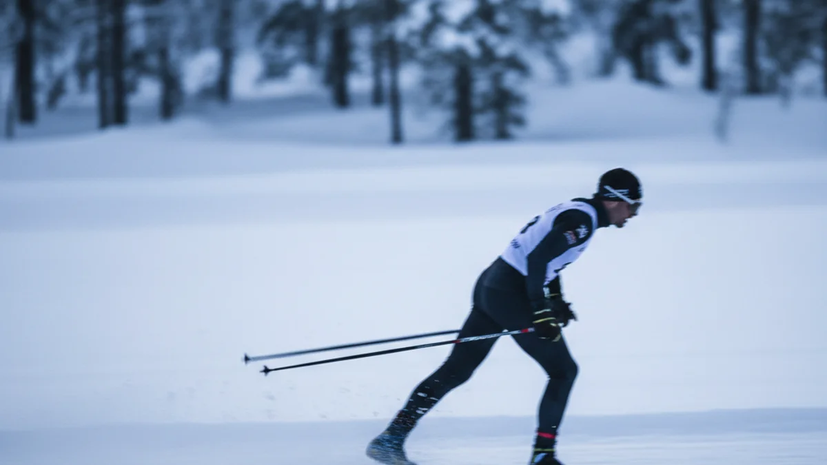 Imatge genèrica d'un esquiador de fons competint en una pista nevada, amb figures borroses al fons.