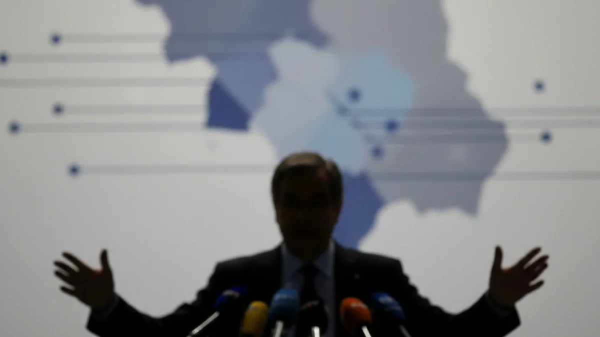 Imatge genèrica d'un polític fent un anunci important en un faristol amb micròfons, sense text visible.