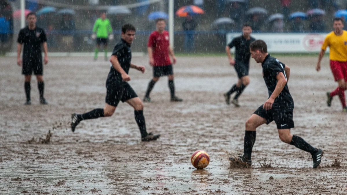 Imatge genèrica d'un partit de futbol local jugat sota una pluja intensa, amb jugadors lluitant per la pilota en un camp enfangat.