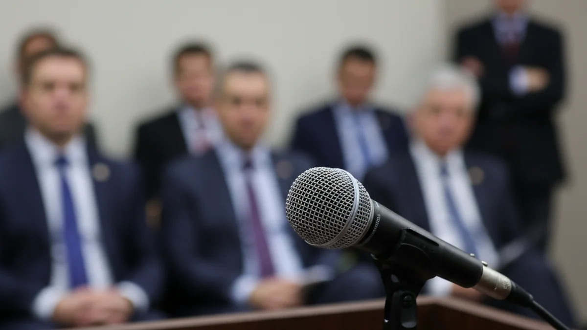 Micròfon en un faristol durant una conferència de premsa política o sindical, amb figures borroses al fons.