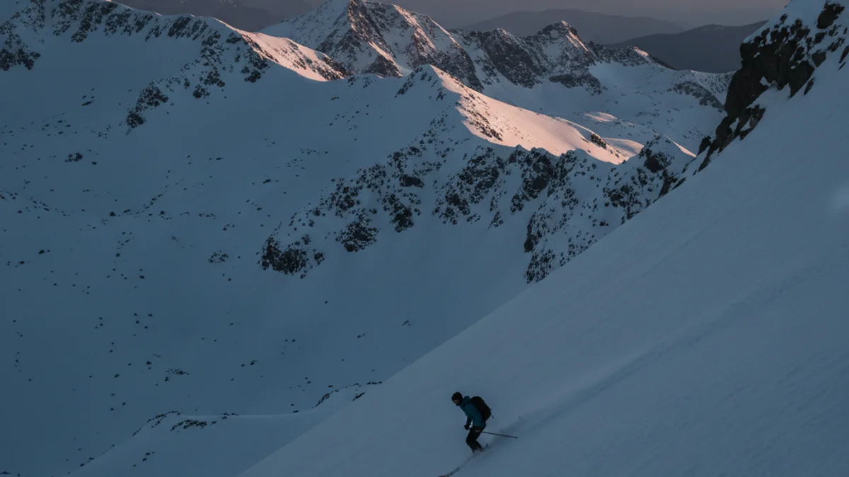 Imatge genèrica d'un jove esportista de freeride baixant per una muntanya nevada, sense cares visibles.