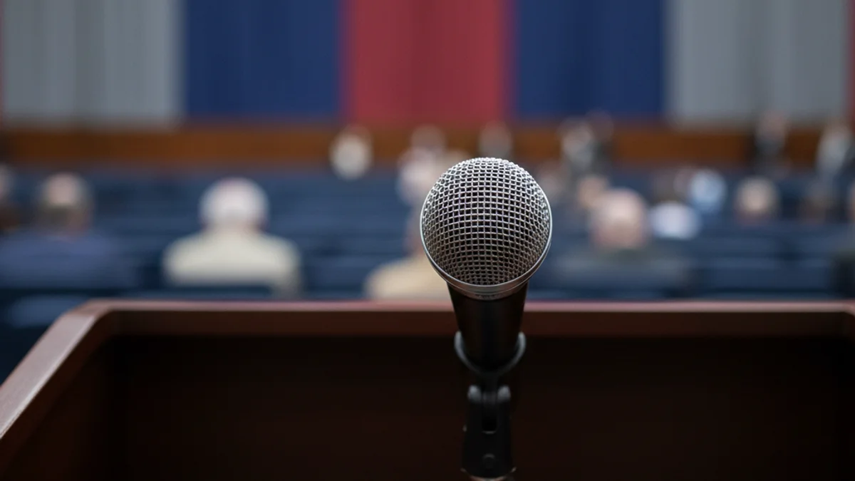 Un micròfon en un faristol buit durant un acte polític amb banderes de partit al fons.