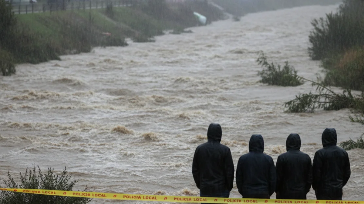 Imatge genèrica d'una riera desbordada durant un temporal de pluja amb llums d'emergència al fons.