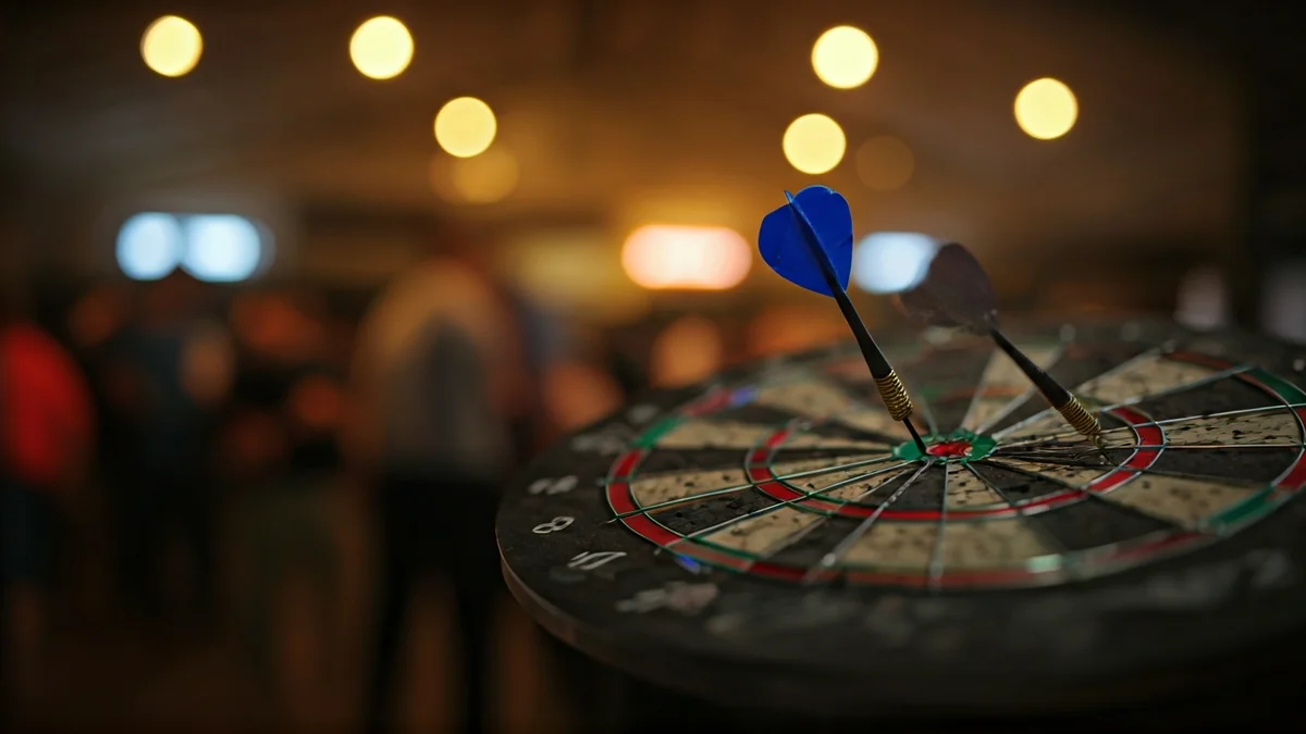 Imagen genérica de una diana con dardos clavados en el centro, con un fondo desenfocado de una sala deportiva.