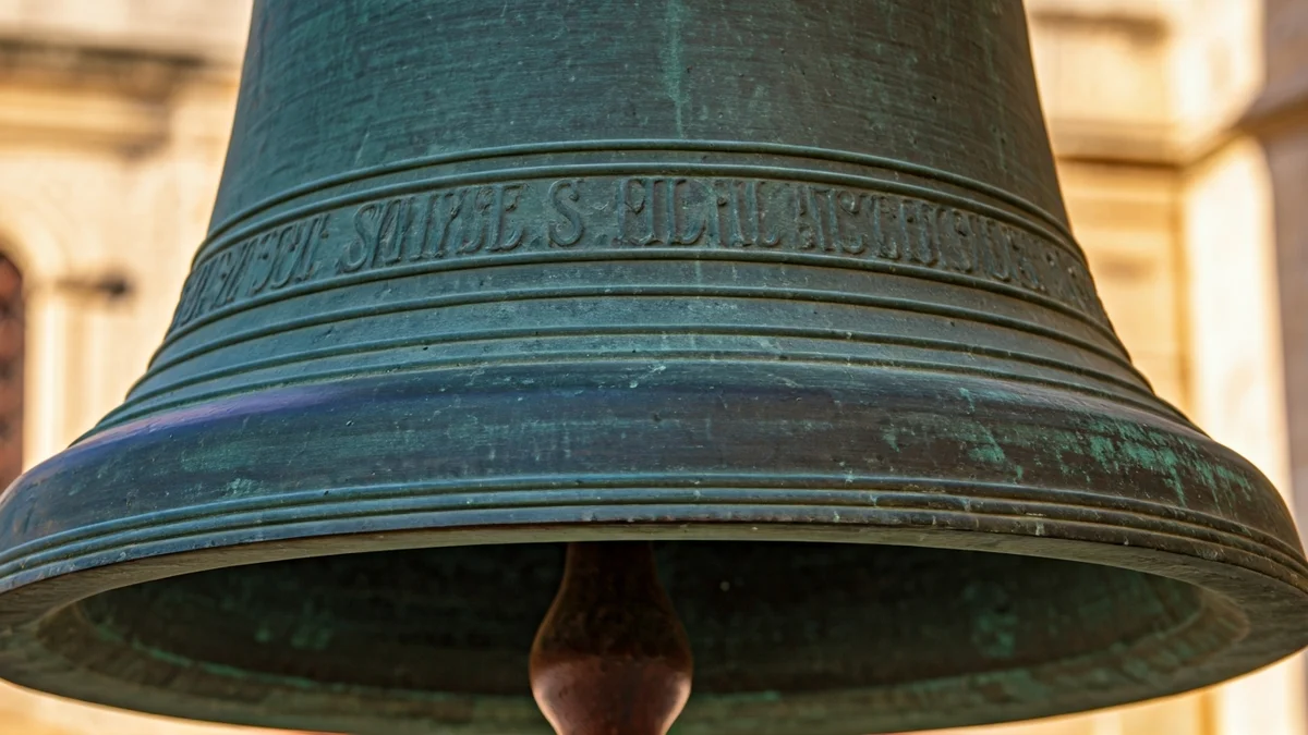 Imatge genèrica d'una campana antiga de bronze amb detalls intricats i pàtina, amb un fons desenfocat d'arquitectura de pedra.