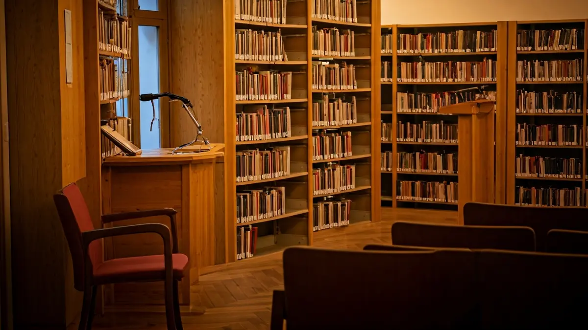 Imatge genèrica d'una biblioteca amb prestatgeries de fusta i un podi amb micròfon, amb una il·luminació càlida.