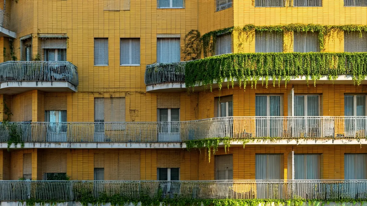Building facade with balconies, windows, and vegetation, featuring yellow ceramics.