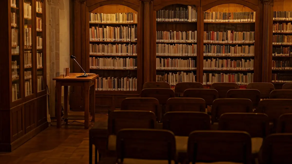 Imatge genèrica d'una biblioteca amb prestatgeries de fusta i un podi amb micròfon, il·luminada càlidament.