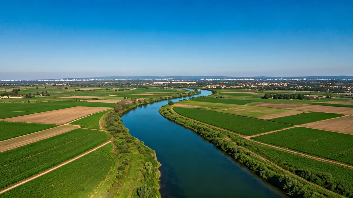 Imatge genèrica d'un riu travessant un paisatge agrícola amb zones urbanes al fons.