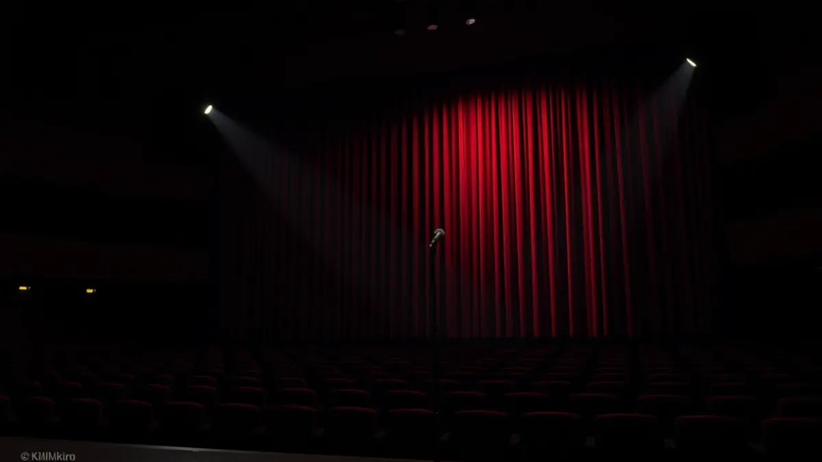 Generic image of a theater stage with a microphone under a spotlight.