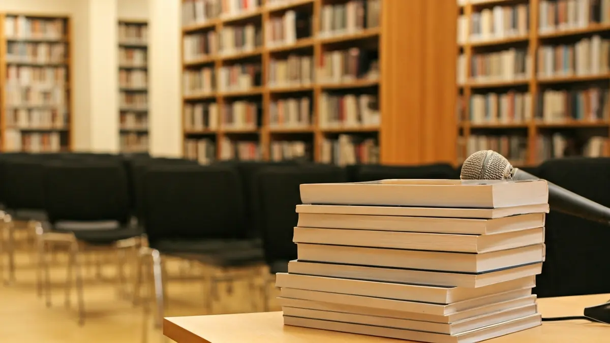 Imatge genèrica d'una biblioteca amb llibres i un micròfon, simbolitzant un acte cultural o literari.