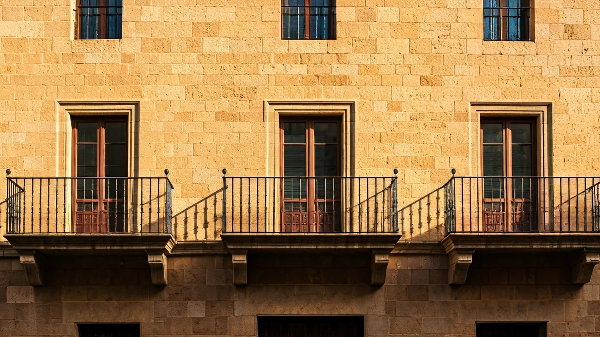 Generic image of a stone town hall facade with a balcony and wrought iron railings, under the afternoon sun.