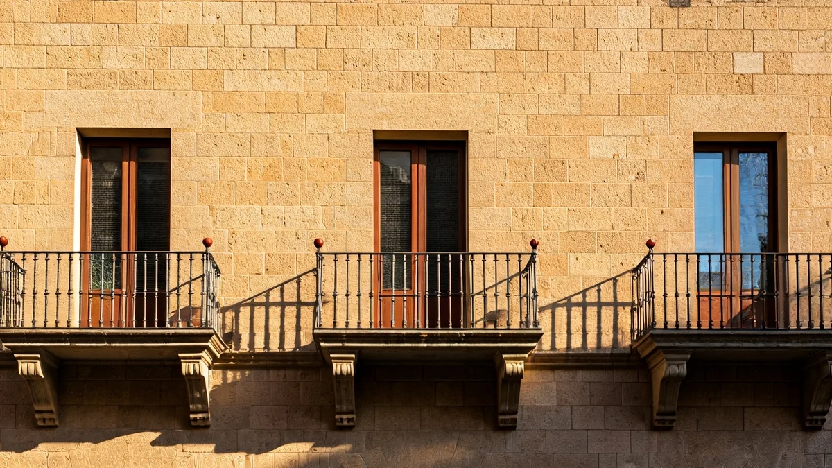 Imagen genérica de una fachada de ayuntamiento de piedra con balcón y barandillas de hierro, bajo la luz del sol mediterráneo.