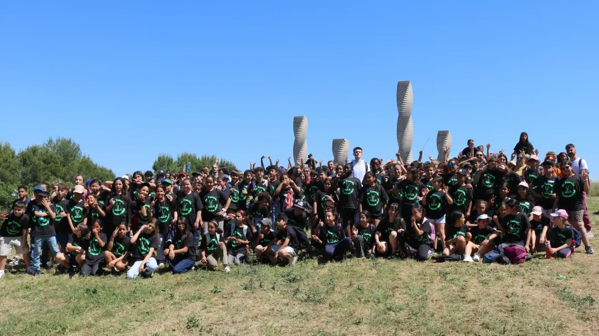 Nens i nenes amb samarretes negres amb el lema 'De l'escola a la universitat' caminen per la gespa d'un campus universitari.