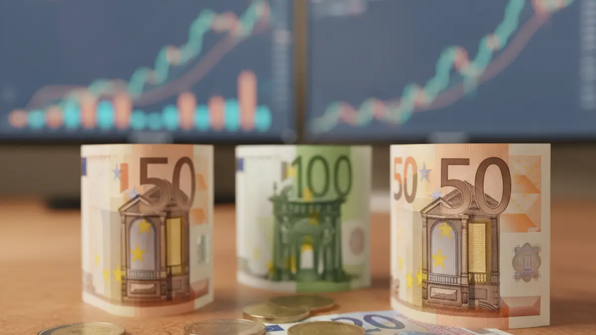 Generic image of coins and banknotes on a desk, with blurred financial charts in the background.