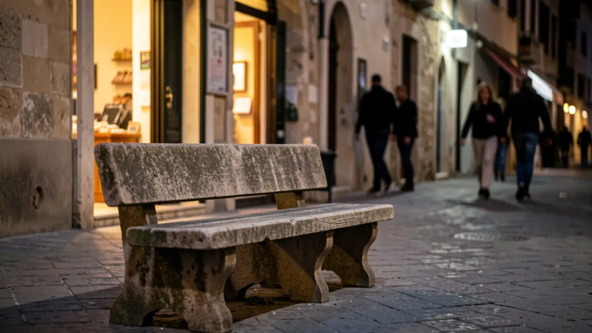 Bench on Mossèn Gudiol street in Vic at night with people talking and listening to music.
