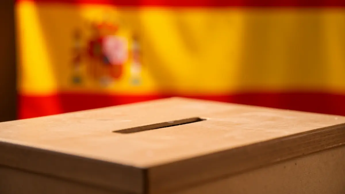 Urna electoral con una bandera española difuminada al fondo.