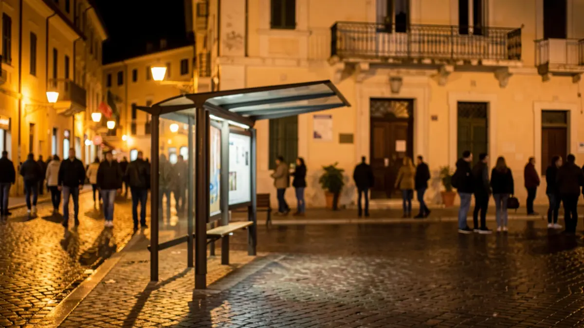 Parada de bus nocturna amb paviment mullat i façana d'un ajuntament al fons.